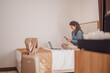 Businesswoman sitting on bed, using laptop talking over phone. Young modern  woman executive on business trip working in  hotel room.