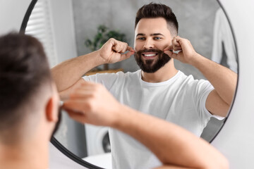 Sticker - Handsome young man touching mustache near mirror in bathroom