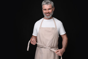 Poster - Happy man wearing kitchen apron on black background. Mockup for design