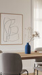 A large, simple line drawing of an abstract shape hangs on the wall above a modern dining table with grey chairs in a minimalistic style with neutral tones and clean lines.