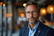 © Gonzalo - Portrait of successful mature boss, senior businessman in glasses and business suit looking at camera and smiling, man with crossed arms working inside modern office building