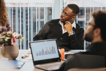 A group of young, mixed-race business professionals engaged in a serious discussion while analyzing statistical data in a modern office meeting room.