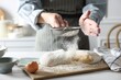 Making dough. Woman sifting flour at white wooden table in kitchen, closeup