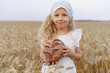 Little beautiful blonde girl with rye bread in a field of ears of rye