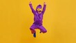 a happy child dressed as a superhero with a purple costume and mask jumps in the air on a yellow background in a wide angle shot