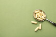 Vitamin capsules in spoon on olive background, top view. Space for text