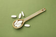 Vitamin pills in spoon on olive background, top view