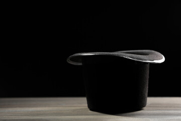 Magician's hat on white wooden table against black background, space for text