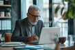 © Nognapas - Confident serious mature businessman using laptop computer, taking notes, working project in modern office. 60 years old female, financier working with documents at workplace. Successful business