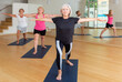 Three mature women doing yoga in a group class perform the exercise by taking the warrior pose II