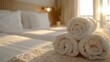 Neatly rolled clean towels arranged on the bed in a bright and welcoming hotel room