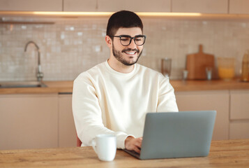 Poster - Cheerful Man Sitting at Table Using Laptop Computer