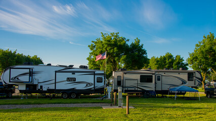 Wall Mural - Fifth wheel trailers parked back to back at campsite on grass with trees and blue cloudy skies