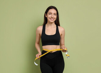 Wall Mural - Happy young woman with measuring tape showing her slim body on green background