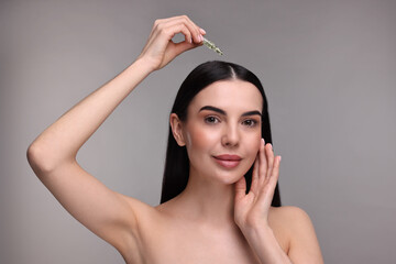 Canvas Print - Beautiful young woman using ampoule for hair treatment on grey background