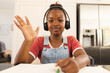 African American girl in headphones, waving on video call at home, doing homework