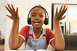 African American girl with headphones, raising hands excitedly at home