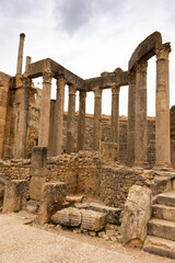 Wall Mural - View of remains of ancient stone stage columns and seating steps of Roman theatre in Dougga against cloudy spring sky. Historical archaeological sites of Tunisia..