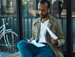 A young black man looks through documents while sitting at a bus stop.