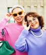 Two happy cheerful pensioner female friends in bright sweaters and sunglasses walk together.