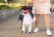 The baby takes the first steps. Mom holds a little girl by the hands and teaches her to walk.
