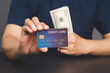 Hand holding a mockup credit card with a dollar bill in the background.