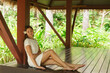 © Acronym - Young and beautiful woman in white dress. Woman posing in exotic Thai bungalow. Resting and traveling concept.