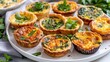 A plate of bitesized quiches and savory tarts perfect for pairing with a nonalcoholic aperitif and reminiscent of classic French cuisine.