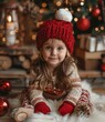 Little girl in red hat sitting by Christmas tree