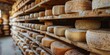 A variety of hard cheeses are on wooden shelves in a warehouse.
