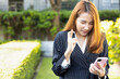 Excited Asian office worker woman showing wishing with finger crossed gesture while looking at smartphone