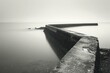 Black and white photo of a long concrete pier jutting out into a calm sea