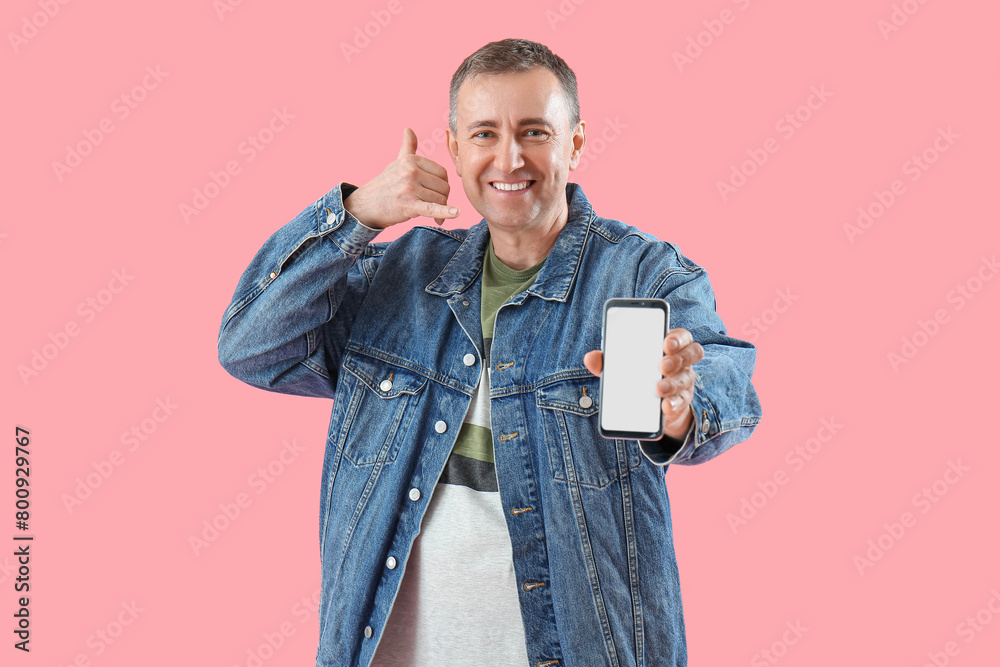 Mature man with mobile phone showing "call me" gesture on pink background