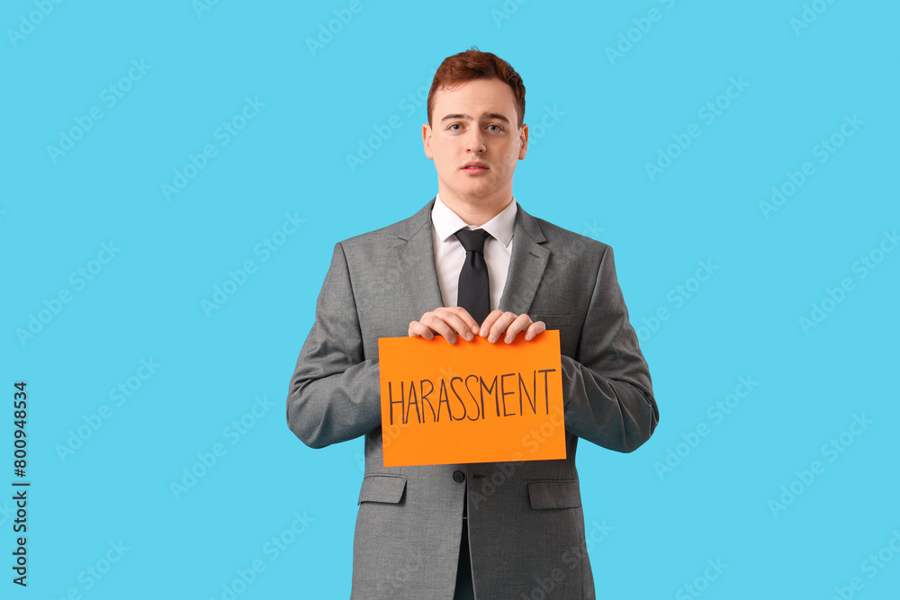Young businessman holding paper with word HARASSMENT on blue background