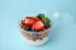 Tasty granola with berries, nuts and yogurt in plastic cup on light blue background, closeup