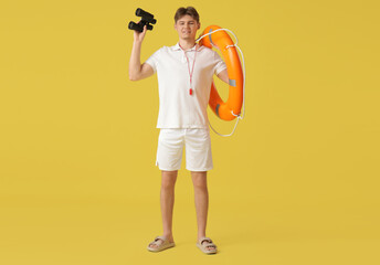 Wall Mural - Male lifeguard with binoculars and lifebuoy ring on yellow background