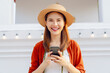 Cheerful beautiful Asian woman holding smartphone and camera with looking for tourist attractions.