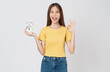 Young asian woman holding alarm clock and shows ok sign on white background studio.