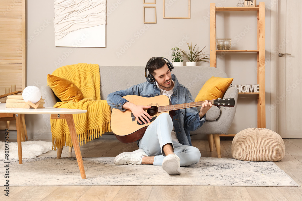 Young bearded man in headphones playing guitar at home