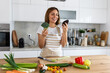 Cute happy young brunette woman in good mood preparing a fresh vegan salad for a healthy life in the kitchen of her home.
