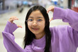 Asian girl with long hair wearing a long-sleeved t-shirt and glasses poses and smiles brightly at the airport.