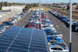 A parking lot features a solar panel roof with several rows of vehicles parked outdoors in a car park by railway.