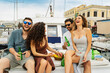 Two happy couples share laughter and drinks during a casual yacht party, epitomizing carefree summer fun at the marina.