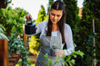One young caucasian woman is taking care of her plants using plant mister and water can