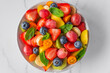 Healthy fresh fruit salad in a bowl on white marble background. Top view. Summer healthy food for breakfast. Mixed fruits, berries and mint for diet lunch