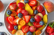 Healthy fresh fruit salad in a bowl on white marble background. Top view. Summer healthy food for breakfast. Mixed tropical fruits berries for vegan diet lunch. Close up
