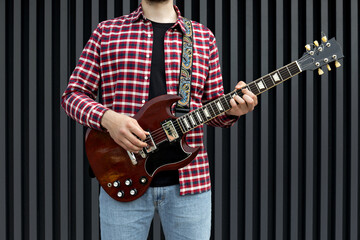 Wall Mural - A stylish young guy plays the guitar on a dark background