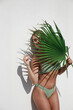 Young Woman in Green Bikini Posing with Palm Leaf on White Background