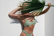 Young Woman in Green Bikini Posing with Palm Leaf on White Background.