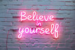 © ALL YOU NEED studio - Neon sign with the words believe in yourself on white brick wall, pink neon light, urban art style. motivational phrase, motivation, affirmation